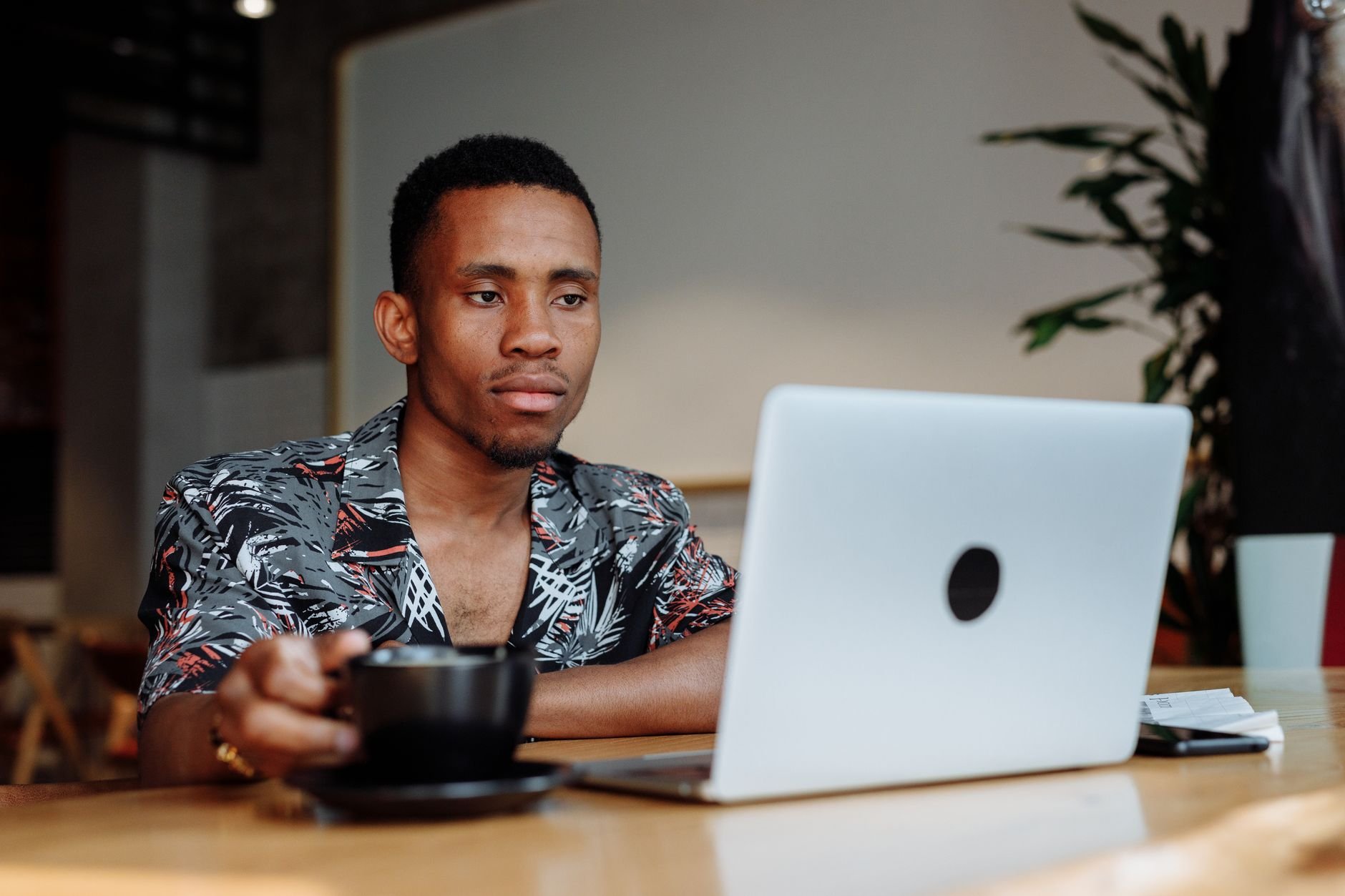 Young man in coffee shop working on laptop with a cup of coffee, modern and relaxed vibe.
